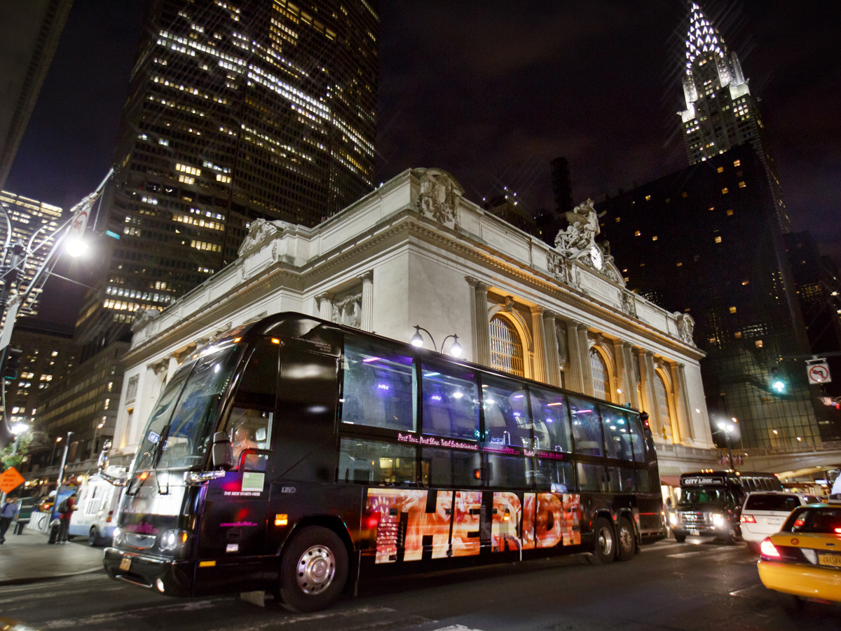 The Ride attraction bus driving on the street in New York City at night.