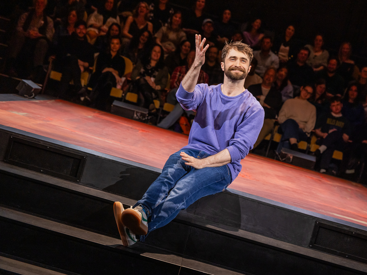 Daniel Radcliffe sits smiling on a stage